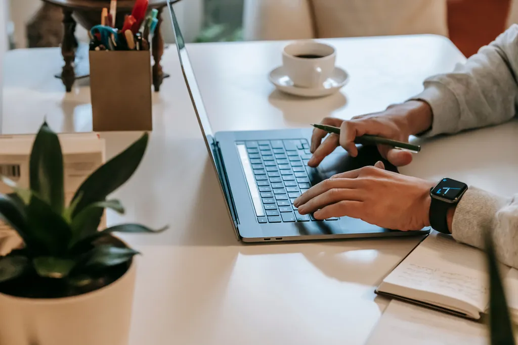 Hands typing on a laptop beside a notepad and a coffee cup