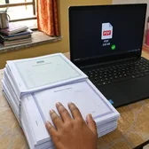 Stack of printed pages beside a laptop showing a PDF icon